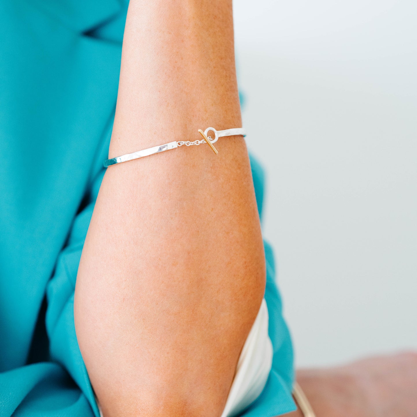 Sterling silver bangle with a connecting chain piece and a yellow gold toggle accent.