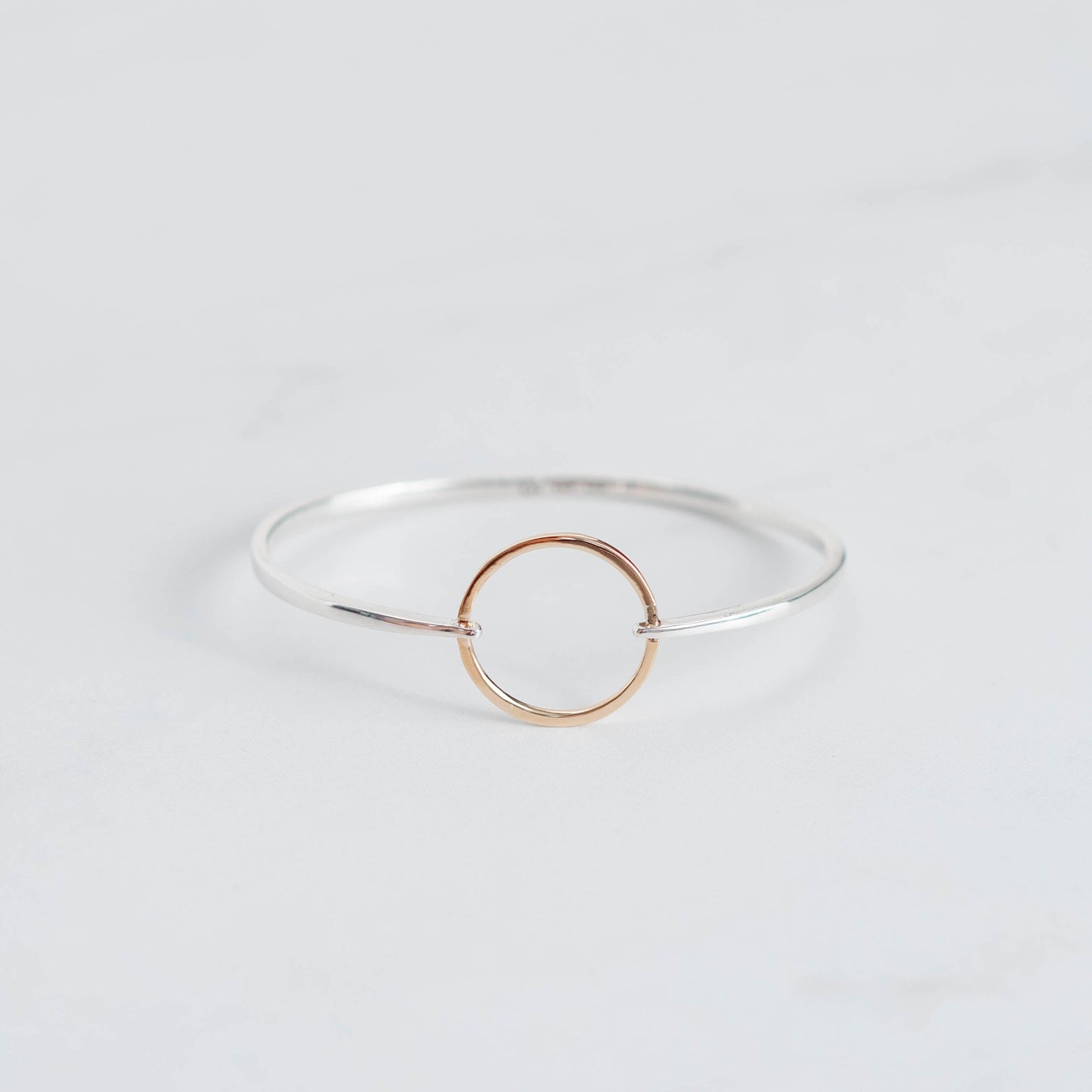 High polished silver bangle with a yellow gold ring connecting it. 