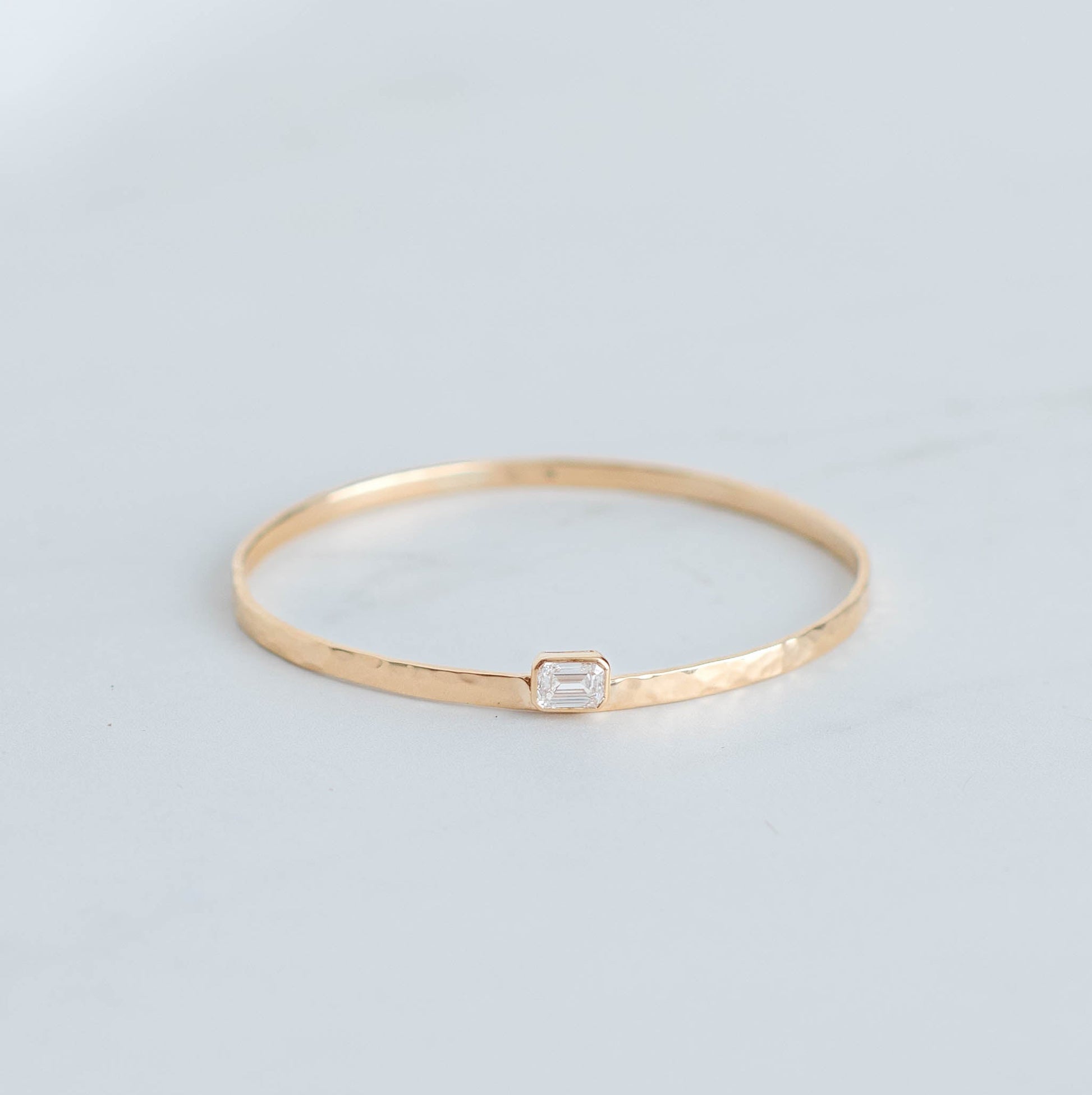 Solid gold bangle with an emerald cut lab grown diamond set in a yellow gold bezel.
