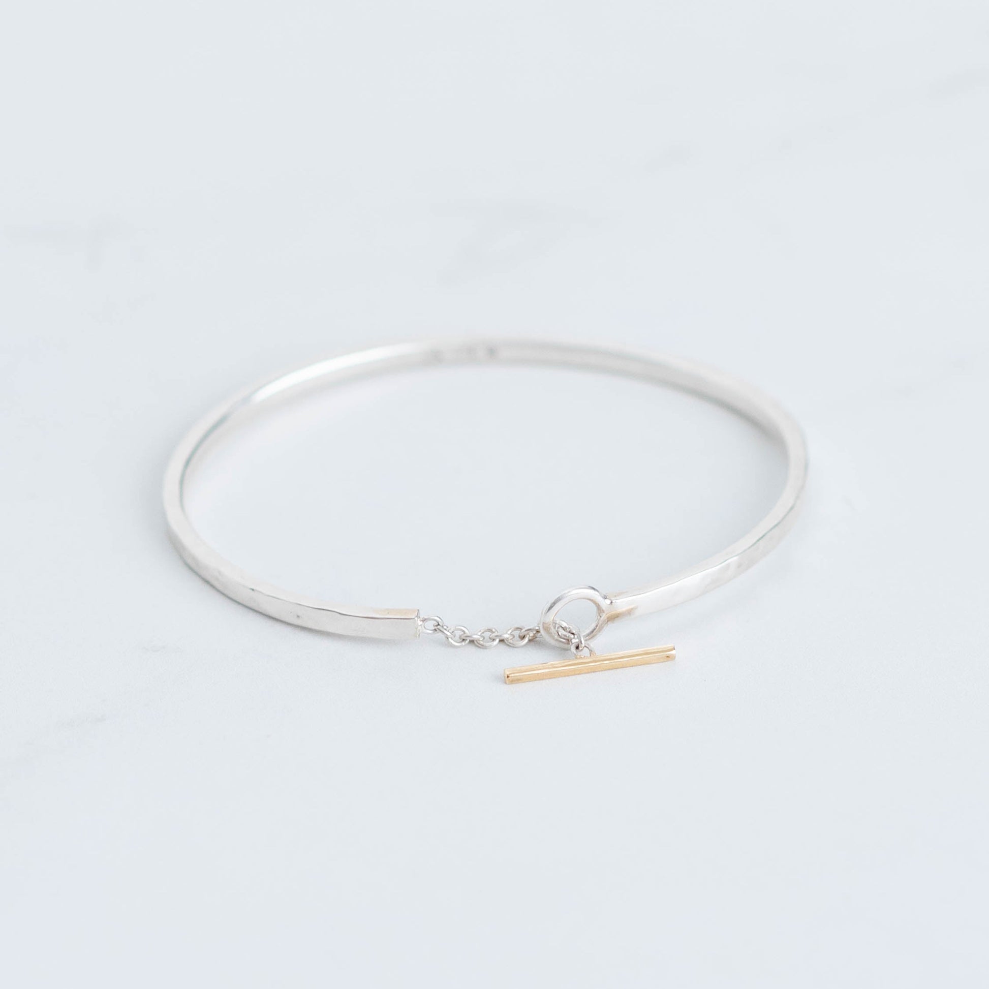 Sterling silver bangle with a connecting chain piece and a yellow gold toggle accent. 