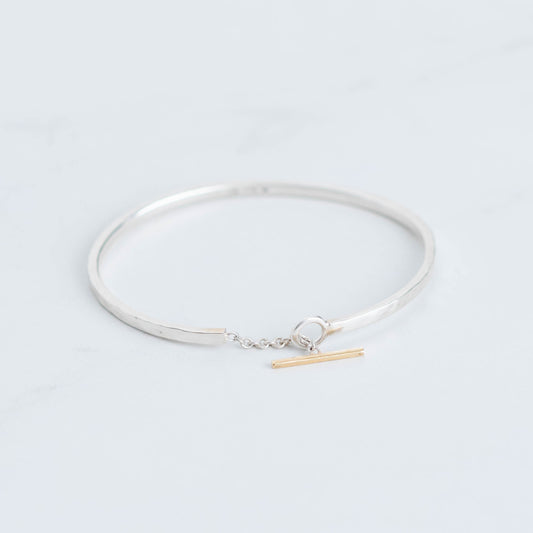 Sterling silver bangle with a connecting chain piece and a yellow gold toggle accent. 