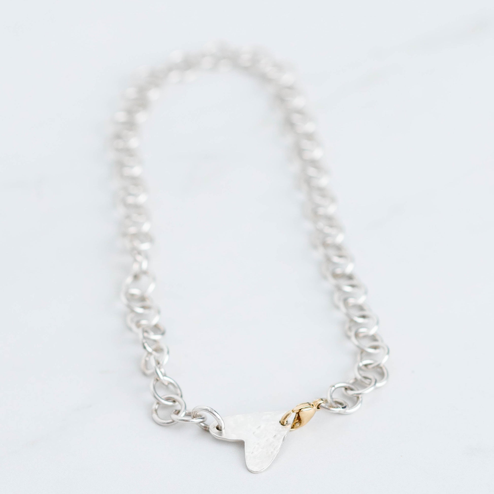 handmade silver chain with a hammered heart pendant and a 10K yellow gold trigger clasp. 