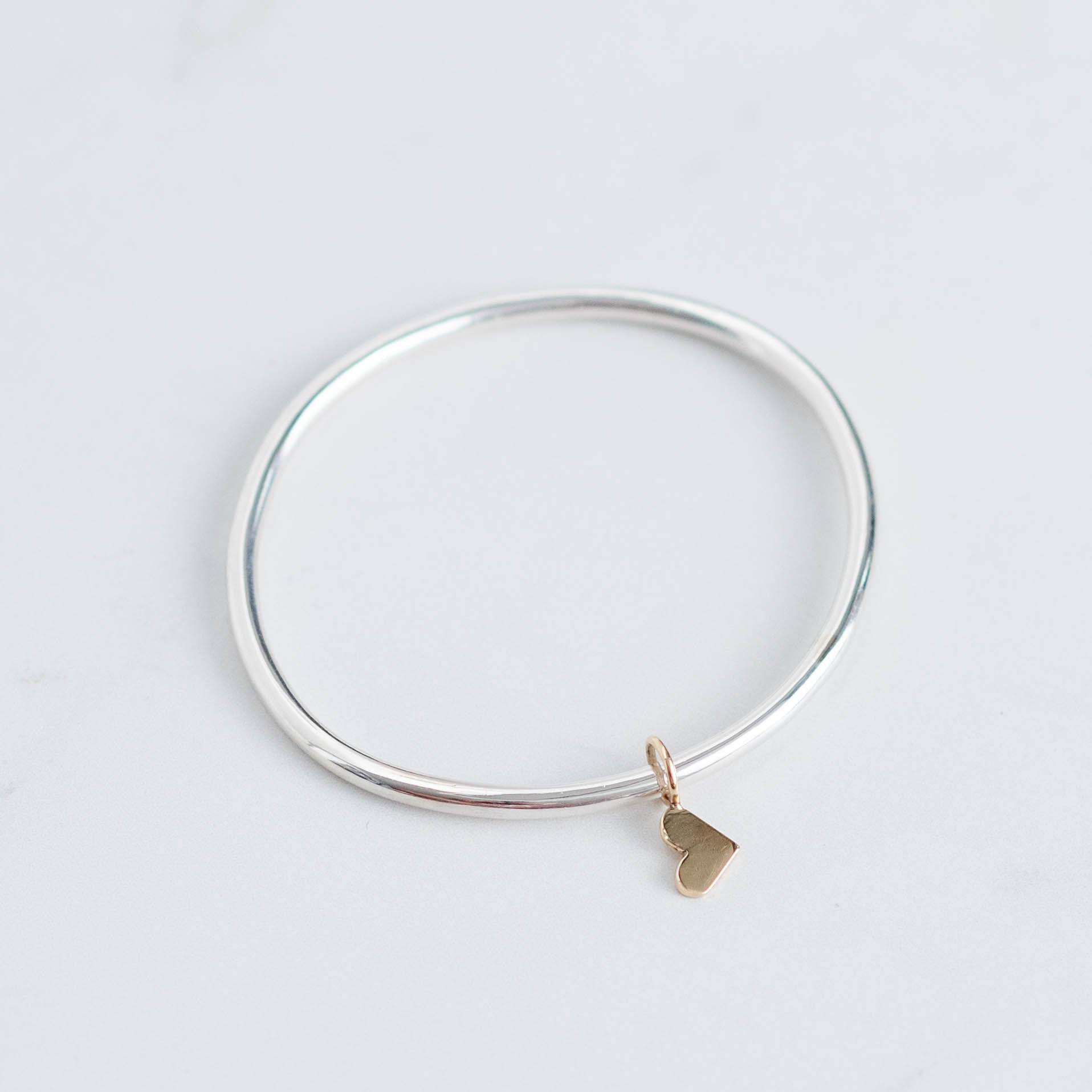 Thick silver bangle with gold dangling heart charm 